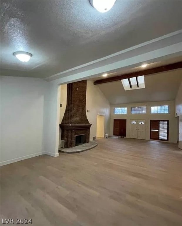 unfurnished living room featuring hardwood / wood-style floors, a fireplace, a textured ceiling, brick wall, and lofted ceiling with skylight