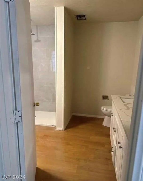 bathroom featuring vanity, toilet, a tile shower, and hardwood / wood-style floors