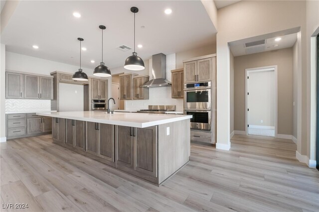 kitchen featuring stainless steel appliances, light hardwood / wood-style flooring, wall chimney range hood, hanging light fixtures, and a large island