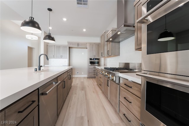 kitchen with sink, decorative light fixtures, light hardwood / wood-style flooring, wall chimney range hood, and appliances with stainless steel finishes