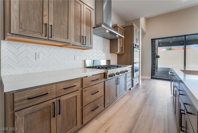 kitchen featuring appliances with stainless steel finishes, wall chimney exhaust hood, tasteful backsplash, and light hardwood / wood-style flooring