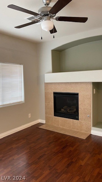 unfurnished living room featuring ceiling fan, a tiled fireplace, and dark wood-type flooring