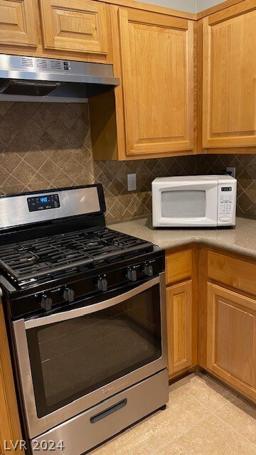 kitchen featuring wall chimney range hood, stainless steel range with gas cooktop, backsplash, and light tile floors