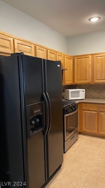 kitchen with black refrigerator with ice dispenser, backsplash, gas range, and light tile floors