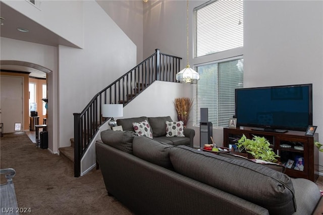 carpeted living area with arched walkways, a towering ceiling, and stairway