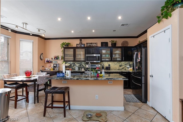 kitchen with dark brown cabinets, a center island with sink, light tile floors, and black refrigerator