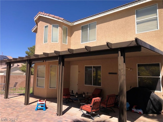 rear view of property featuring stucco siding, fence, a pergola, a tiled roof, and a patio