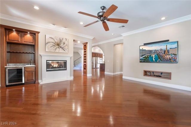 unfurnished living room featuring sink, wine cooler, ceiling fan, ornamental molding, and dark hardwood / wood-style flooring