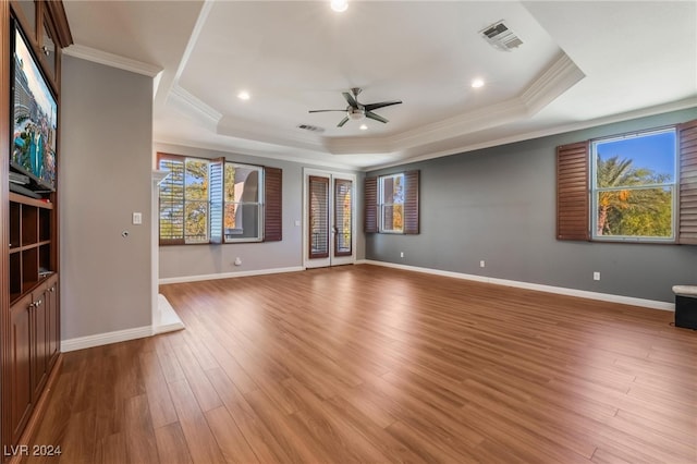 unfurnished living room with ceiling fan, light wood-type flooring, crown molding, and a tray ceiling