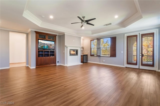 unfurnished living room with a tray ceiling, plenty of natural light, ornamental molding, and hardwood / wood-style flooring