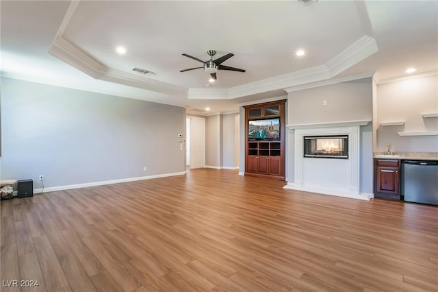 unfurnished living room with a multi sided fireplace, a tray ceiling, light hardwood / wood-style flooring, and crown molding