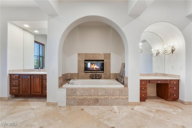 bathroom featuring tiled tub, a fireplace, and vanity