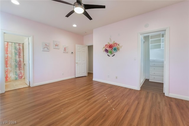 unfurnished bedroom featuring a walk in closet, ensuite bath, ceiling fan, wood-type flooring, and a closet