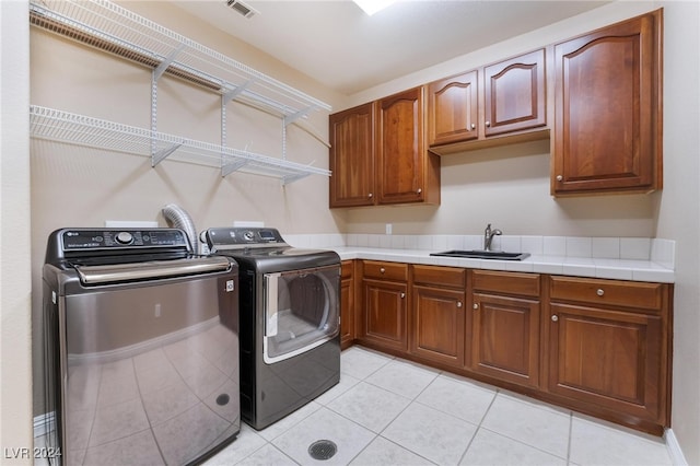 clothes washing area with light tile patterned flooring, cabinets, sink, and washing machine and clothes dryer