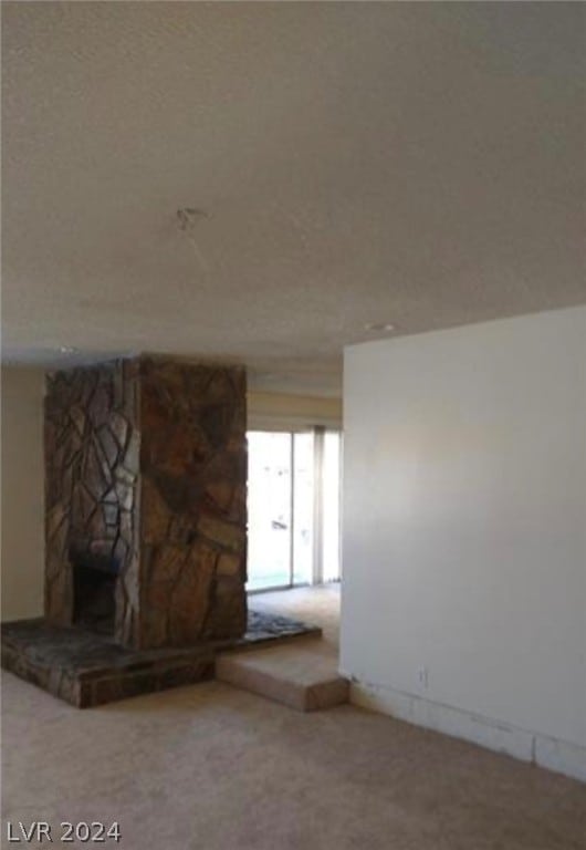 unfurnished living room featuring a stone fireplace and carpet floors