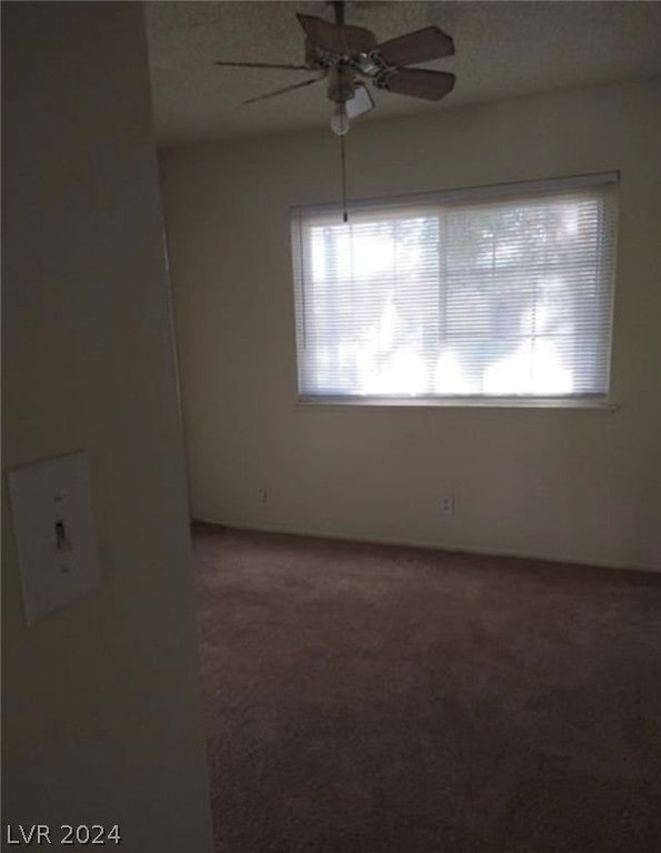 empty room with ceiling fan and dark colored carpet