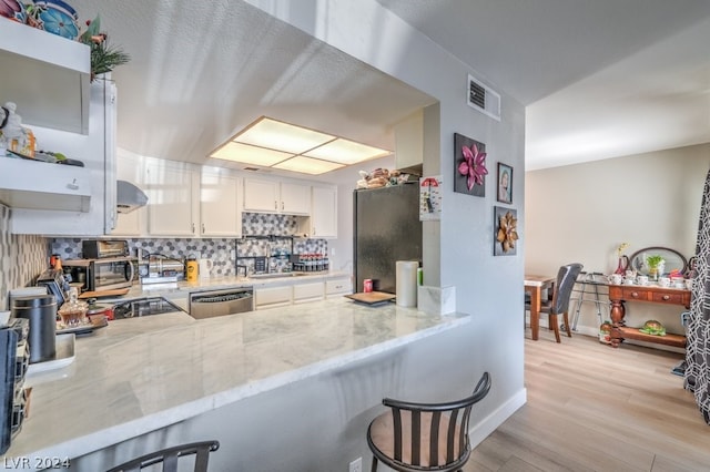 kitchen with light stone countertops, kitchen peninsula, stainless steel appliances, light hardwood / wood-style flooring, and white cabinets