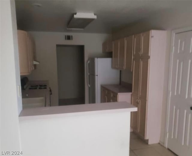 kitchen featuring range, white fridge, light tile flooring, and kitchen peninsula