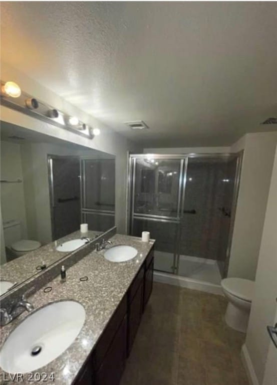 bathroom with double sink, toilet, an enclosed shower, and vanity with extensive cabinet space