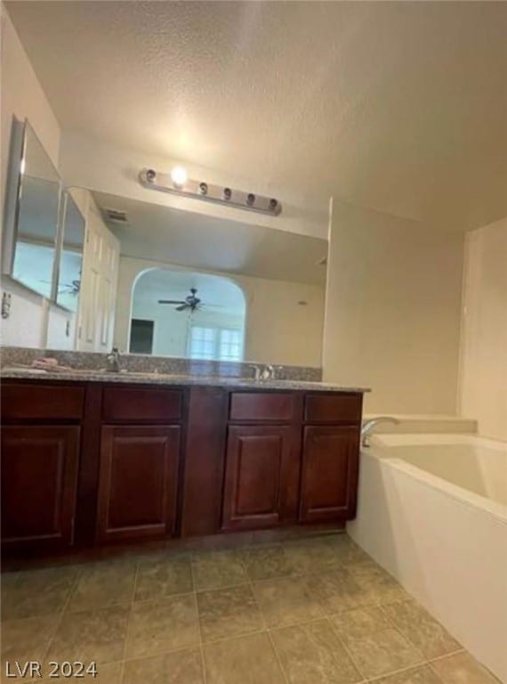 bathroom featuring ceiling fan, a textured ceiling, dual bowl vanity, tile flooring, and a tub