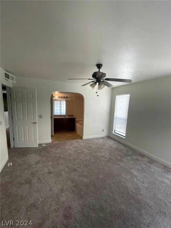 unfurnished living room featuring ceiling fan, dark colored carpet, and a healthy amount of sunlight