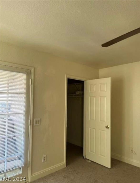 unfurnished bedroom featuring ceiling fan, a closet, dark carpet, and a textured ceiling