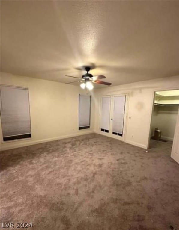 unfurnished bedroom featuring a spacious closet, ceiling fan, a closet, and dark colored carpet