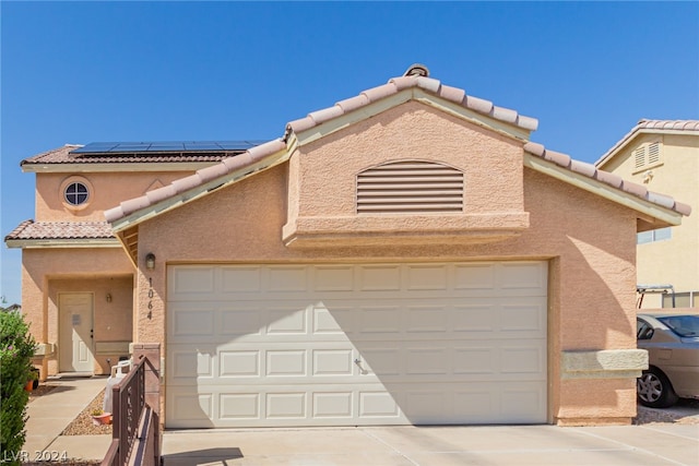 view of front of property featuring a garage, driveway, a tile roof, roof mounted solar panels, and stucco siding