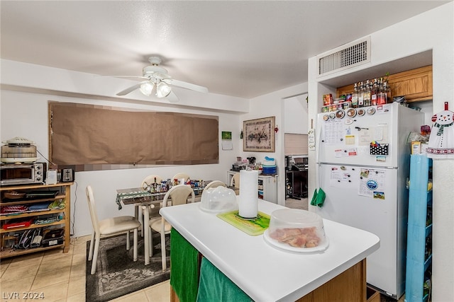 kitchen with light tile patterned floors, visible vents, ceiling fan, a kitchen island, and freestanding refrigerator