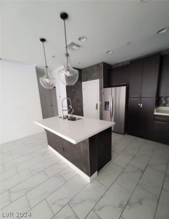 kitchen with pendant lighting, light tile floors, sink, stainless steel refrigerator with ice dispenser, and a center island with sink