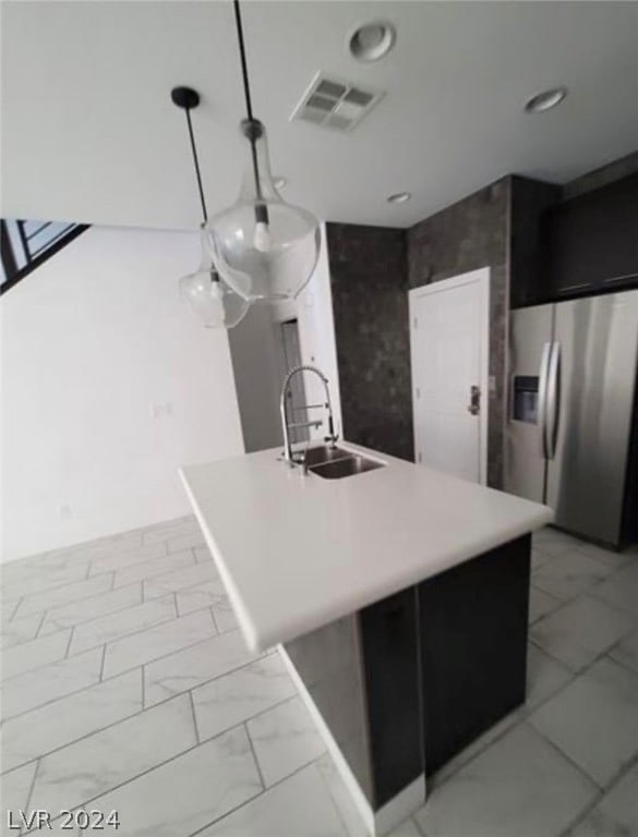 kitchen featuring light tile flooring, hanging light fixtures, stainless steel fridge, sink, and a kitchen island with sink