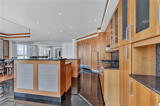 kitchen featuring a center island with sink, dark stone countertops, stainless steel gas cooktop, crown molding, and sink