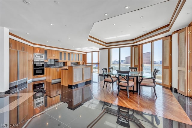 interior space featuring a kitchen island, hardwood / wood-style flooring, built in appliances, a tray ceiling, and crown molding