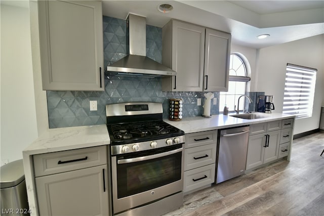 kitchen with light hardwood / wood-style floors, tasteful backsplash, appliances with stainless steel finishes, wall chimney exhaust hood, and sink