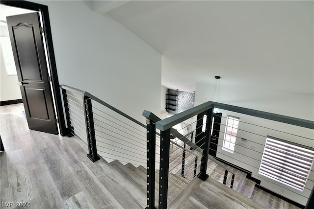 stairway with light hardwood / wood-style flooring and lofted ceiling with beams