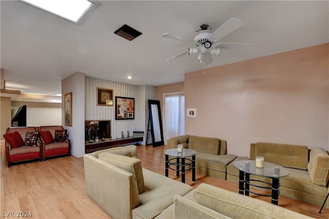 living room featuring light hardwood / wood-style floors, ceiling fan, and a textured ceiling