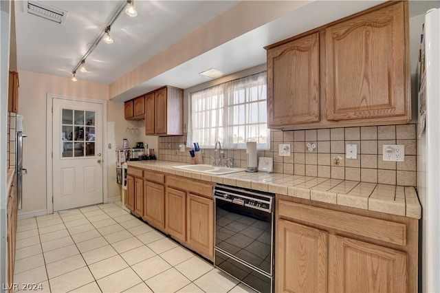 kitchen featuring light tile floors, sink, black dishwasher, rail lighting, and tile countertops