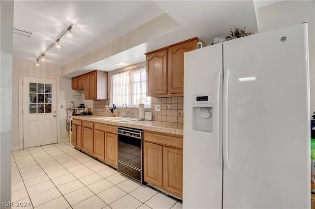 kitchen featuring sink, dishwasher, backsplash, tile countertops, and white refrigerator with ice dispenser