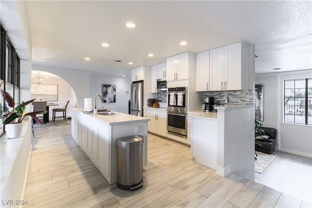 kitchen featuring sink, white cabinets, decorative backsplash, stainless steel appliances, and a center island with sink