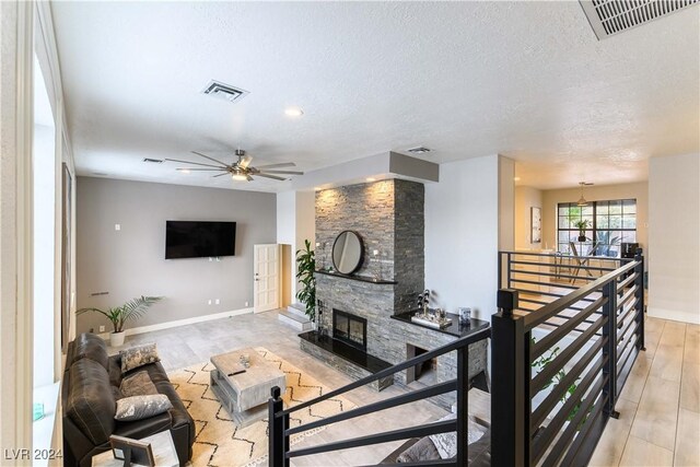 living room featuring light hardwood / wood-style flooring, ceiling fan, a fireplace, and a textured ceiling