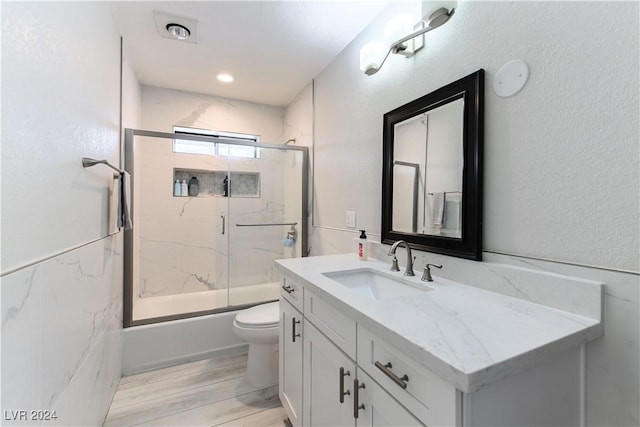 full bathroom with enclosed tub / shower combo, tile walls, hardwood / wood-style floors, vanity, and toilet