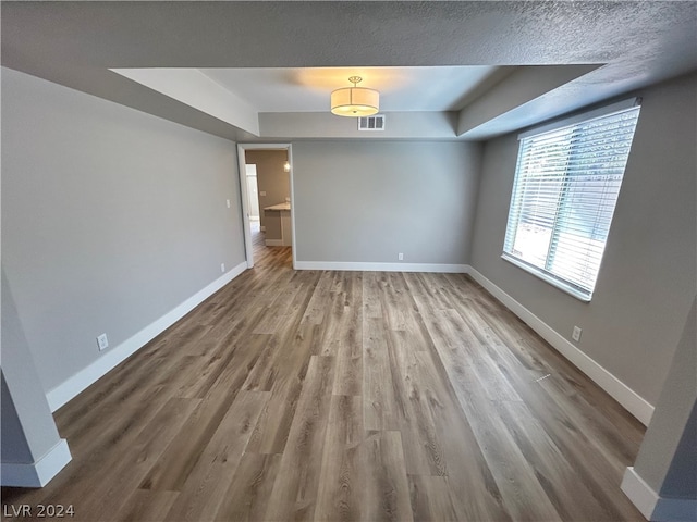 spare room featuring hardwood / wood-style flooring, a textured ceiling, and a raised ceiling