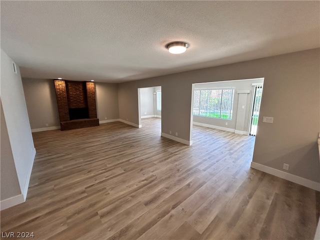 unfurnished living room featuring a fireplace, hardwood / wood-style floors, brick wall, and a textured ceiling