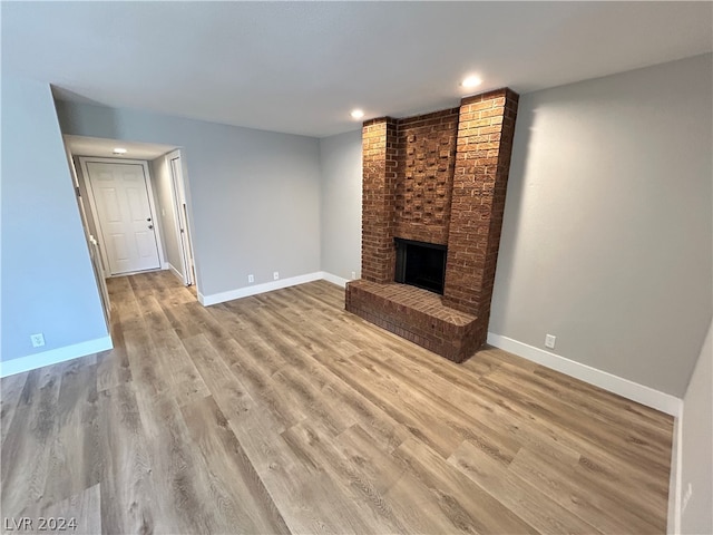 unfurnished living room featuring light hardwood / wood-style floors, brick wall, and a brick fireplace