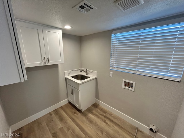 laundry room featuring light hardwood / wood-style flooring, a wealth of natural light, sink, cabinets, and a textured ceiling