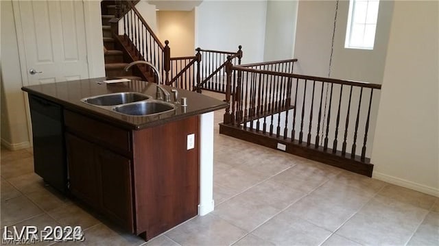 kitchen with light tile floors, black dishwasher, a center island with sink, dark brown cabinetry, and sink