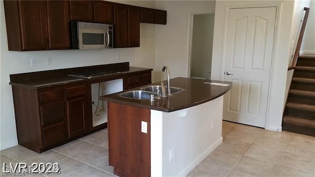 kitchen featuring a kitchen island with sink, sink, black electric stovetop, and light tile floors