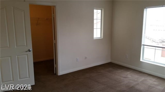 unfurnished bedroom featuring multiple windows, a spacious closet, dark carpet, and a closet