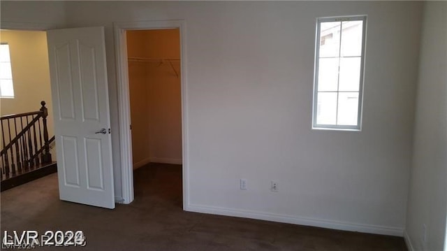 unfurnished bedroom featuring a walk in closet, a closet, and dark colored carpet