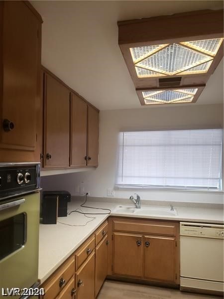 kitchen featuring white dishwasher, stainless steel oven, sink, and light wood-type flooring